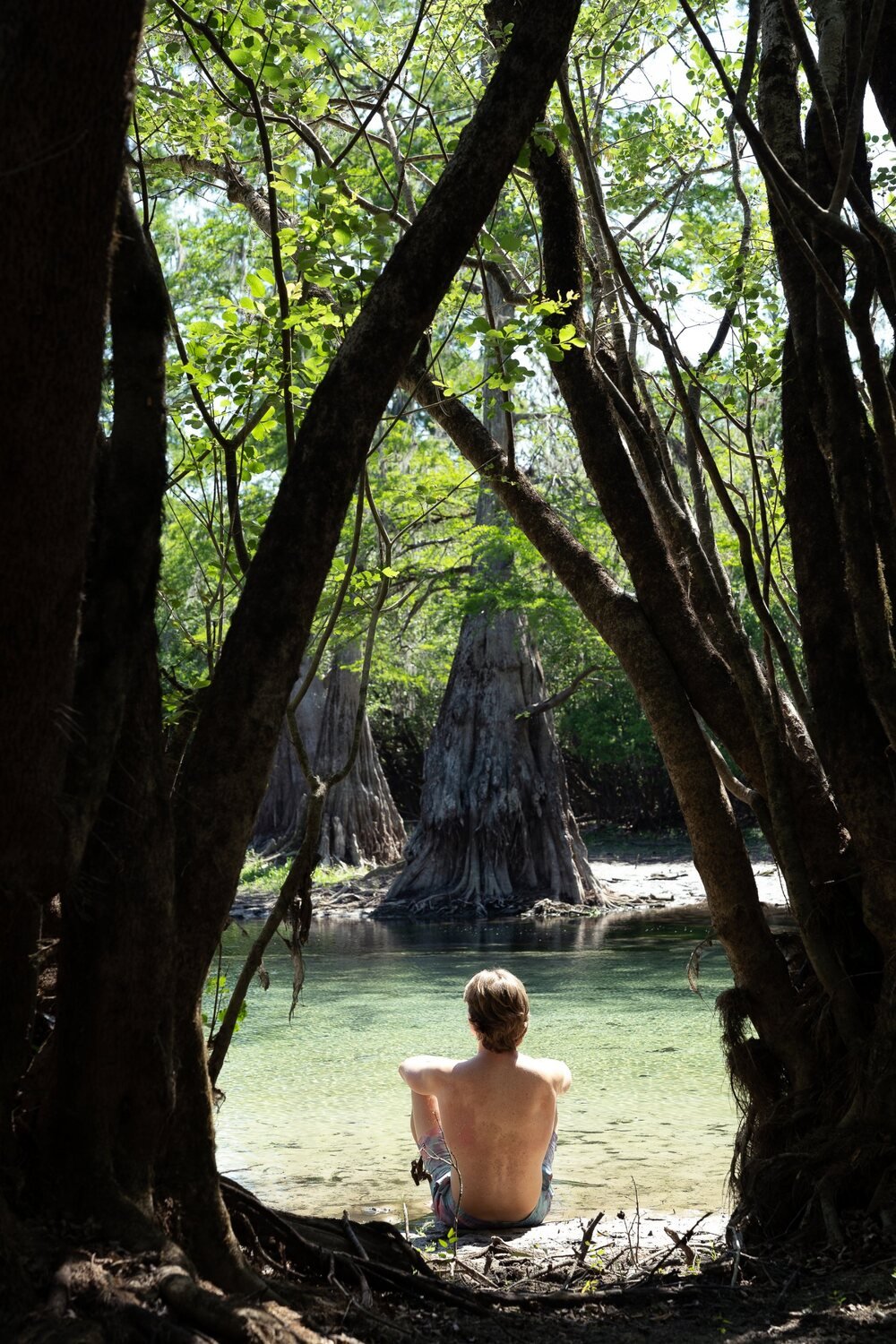Brandon sitting at the edge of a clear Florida spring beneath cypress trees