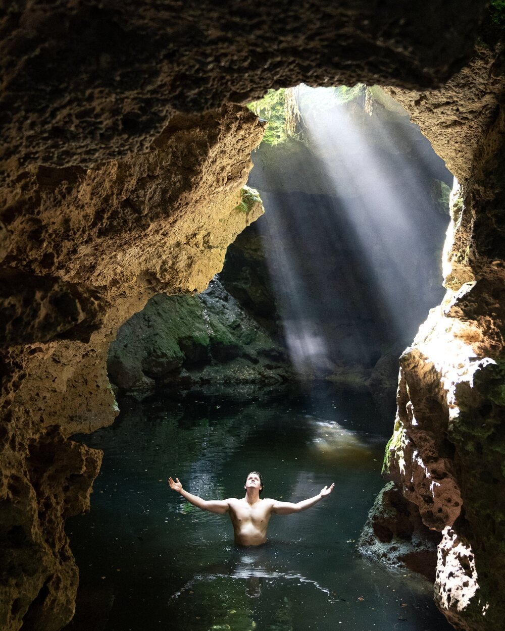 Brandon in a cave spring, arms open beneath a beam of light